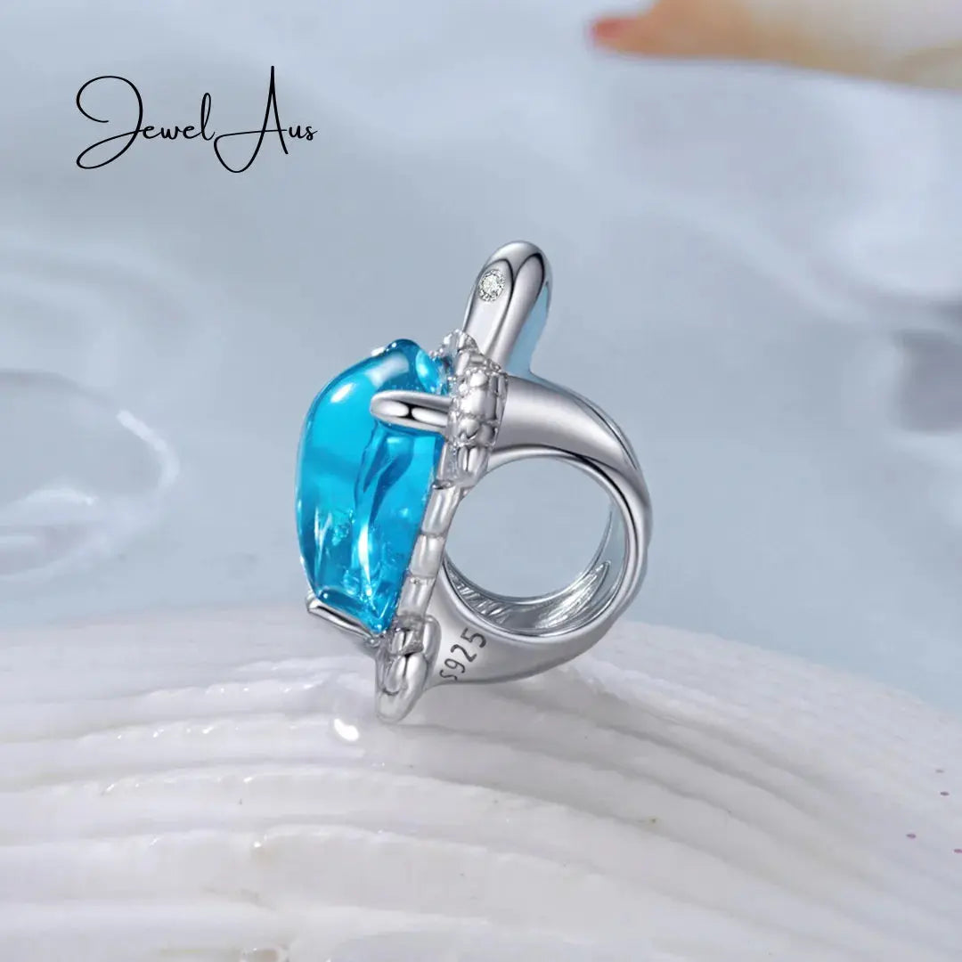 Silver ring with a blue gemstone on a white shell background, featuring the brand 'Jewel Aus'.