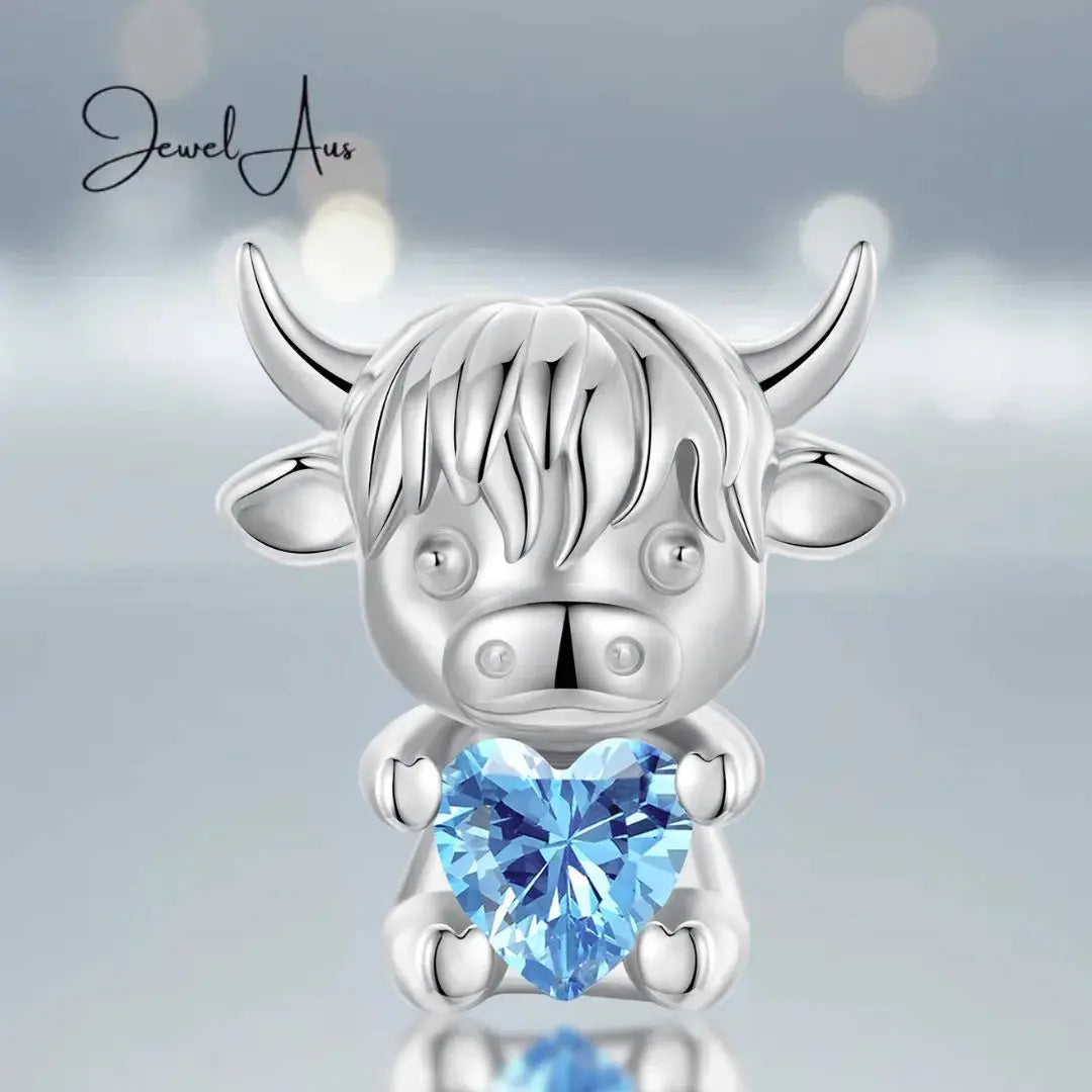 Silver cow-shaped pendant with a blue heart gem on a light gray background