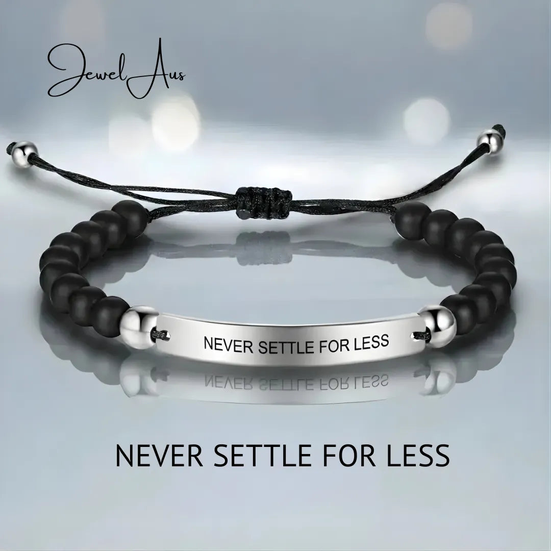 Black beaded bracelet with silver tag on a light gray background, featuring the text 'Never Settle For Less'.