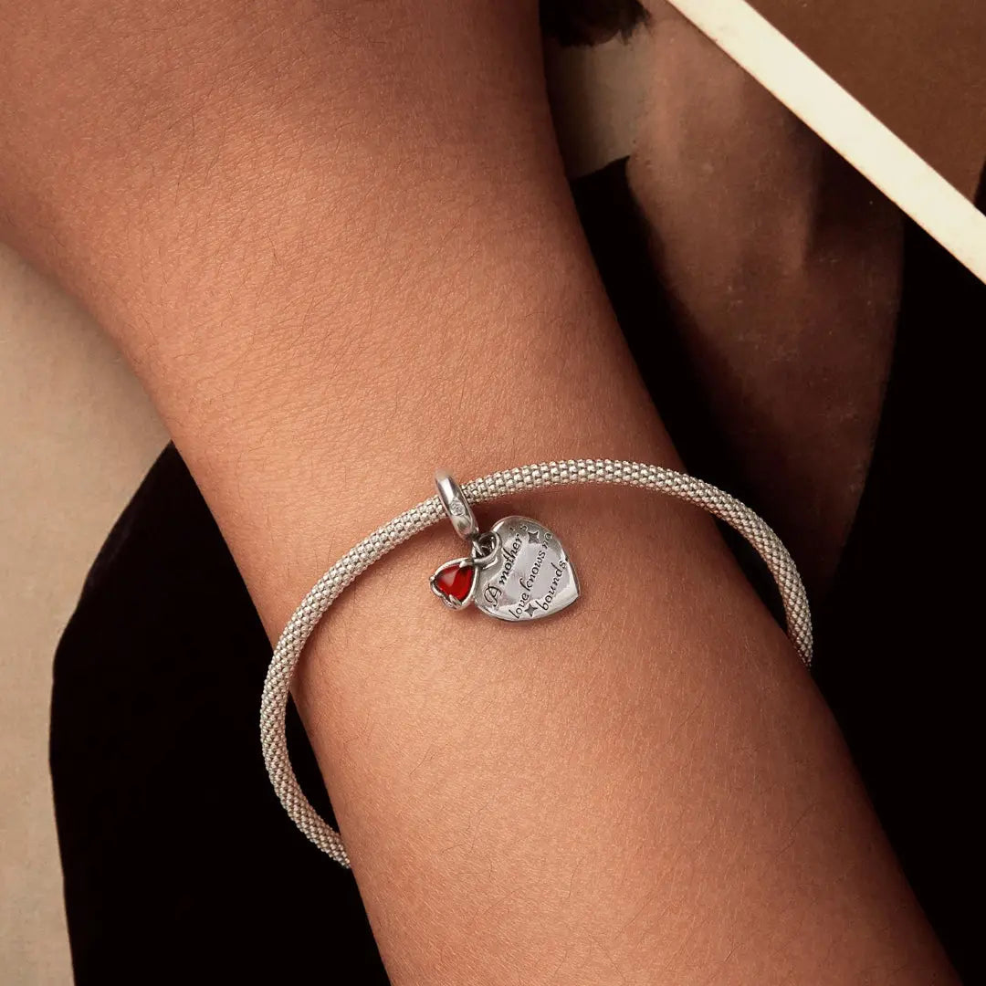 Bracelet with a heart-shaped charm on a wrist against a neutral background