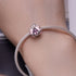 Silver bracelet with a pink gemstone on a wrist, with a magazine in the background.