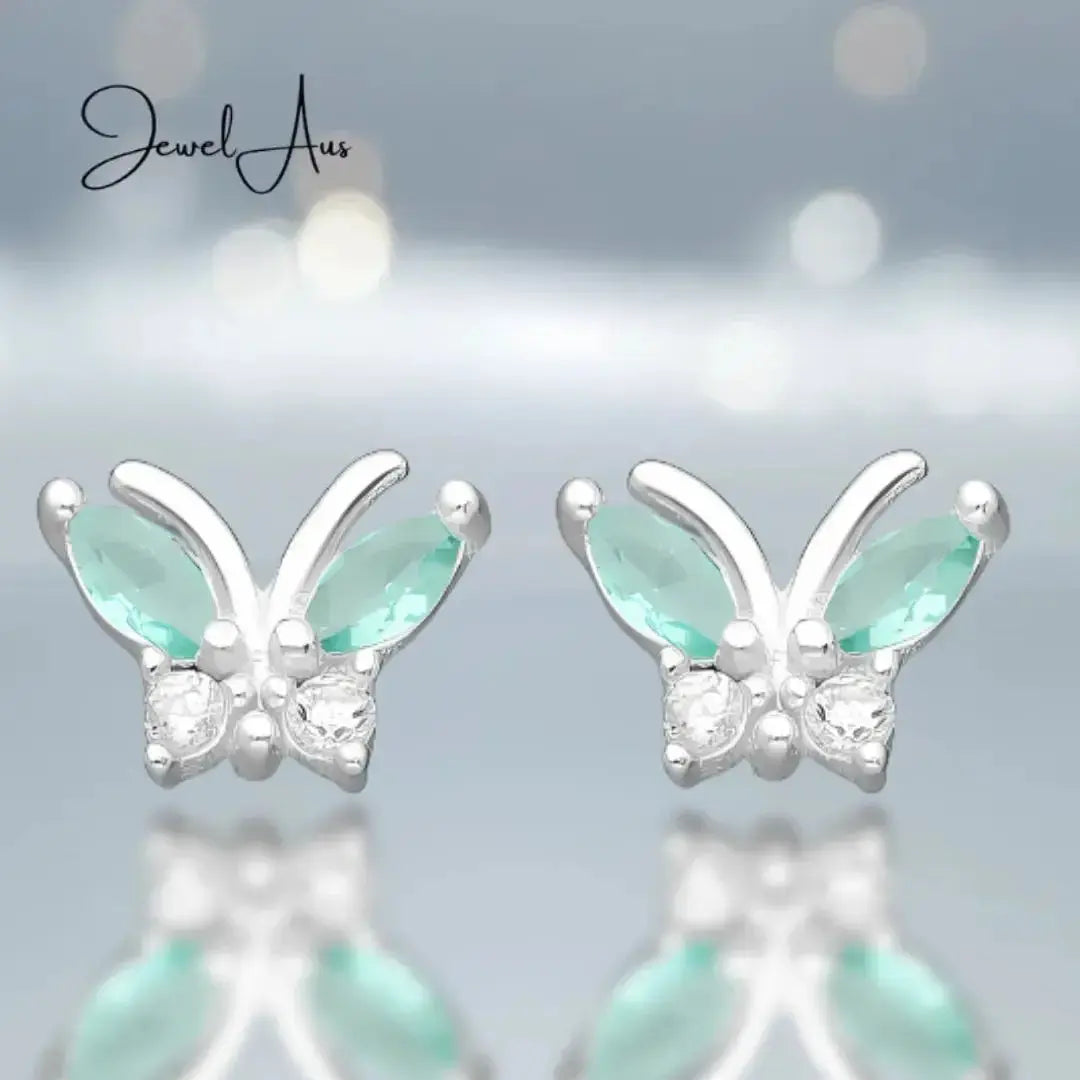 Butterfly-shaped earrings with green gemstones on a blurred background