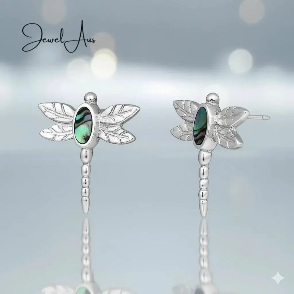 Dragonfly-shaped earrings with green gemstones on a light blue background, branded 'Jewel Aux'.