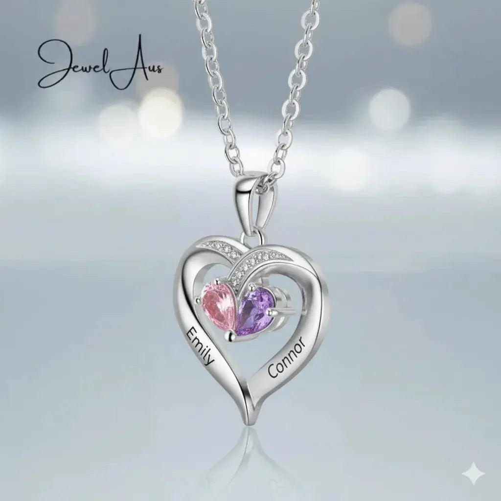 Heart-shaped silver necklace with two colored stones on a light gray background, featuring the brand 'Jewel Aux'.