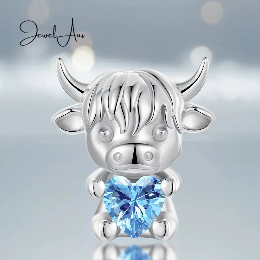 Silver cow-shaped pendant with a blue heart gem on a light gray background