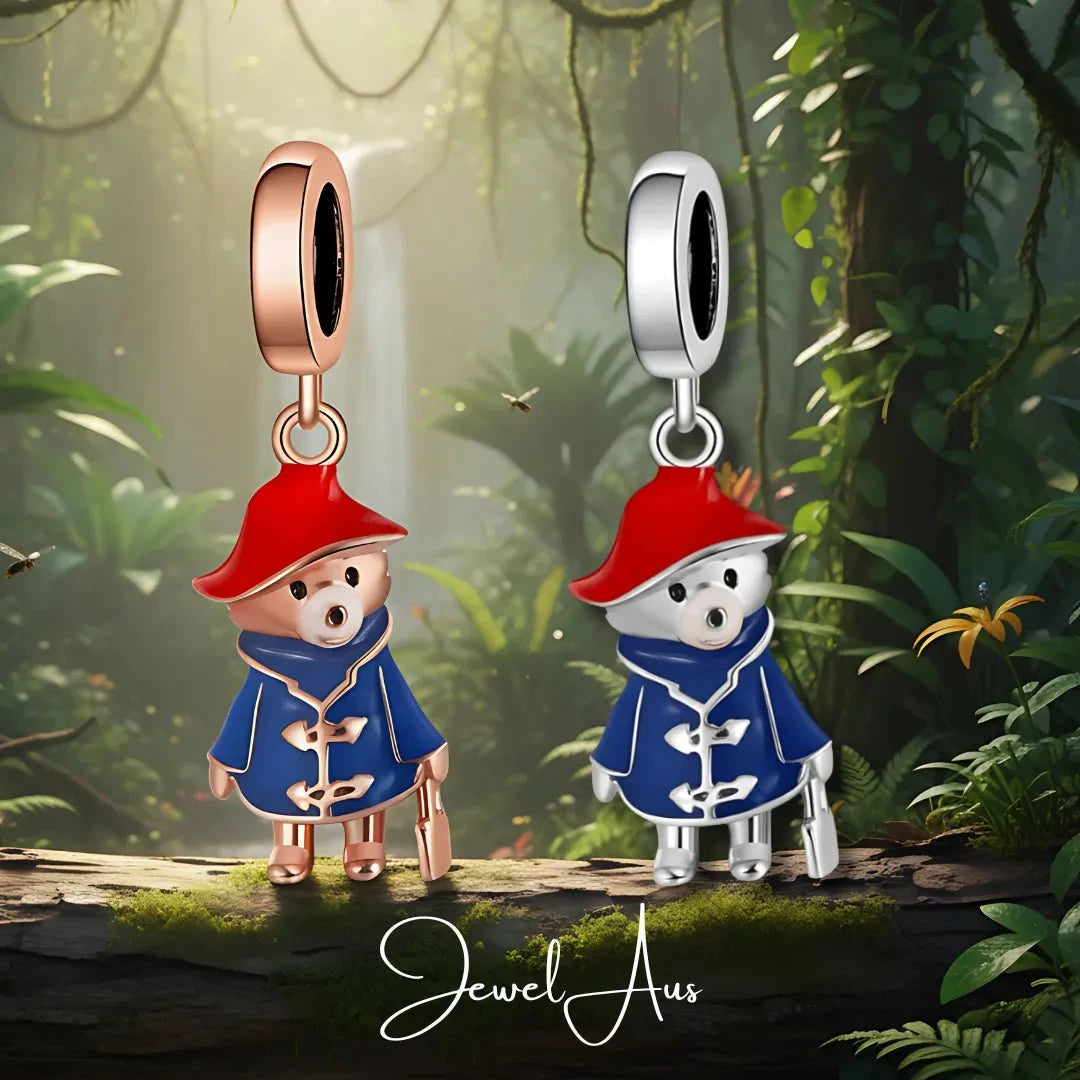 Two bear-shaped charms in red hats and blue coats on a forest background, with 'Jewel Aus' branding.